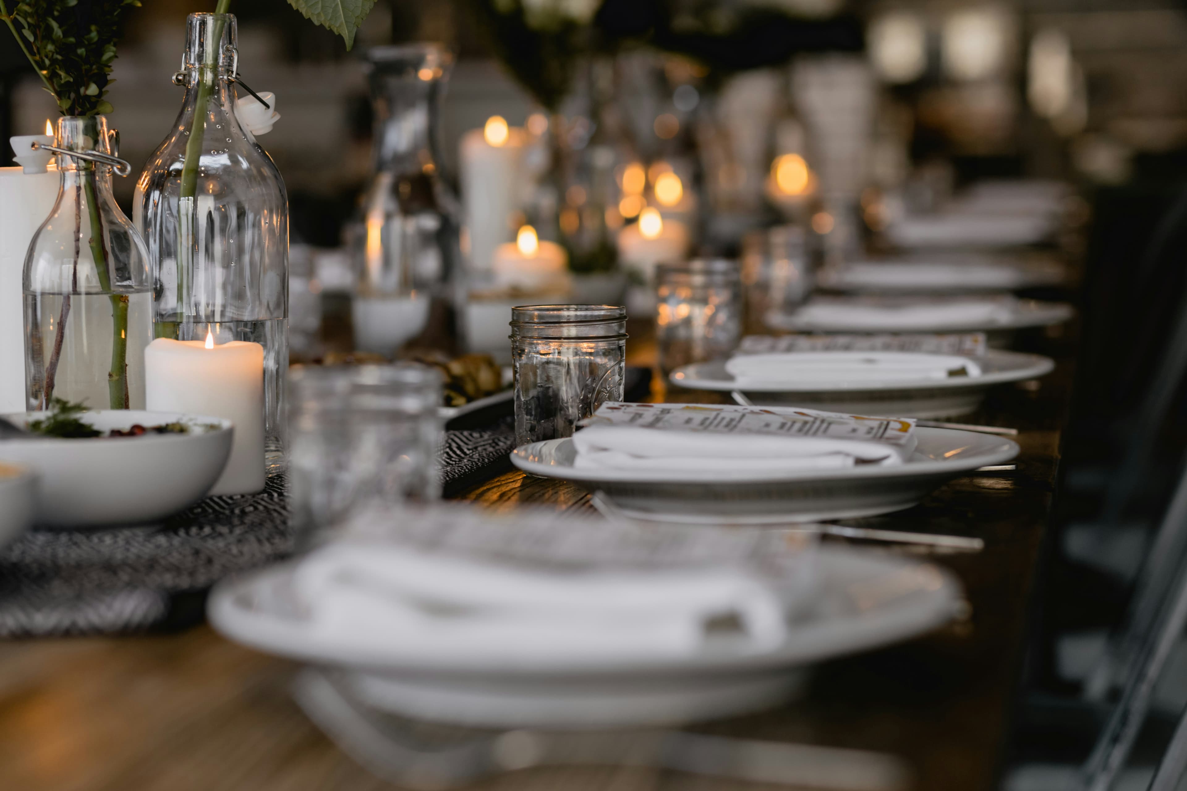 A long dinner table set with white plates and candles