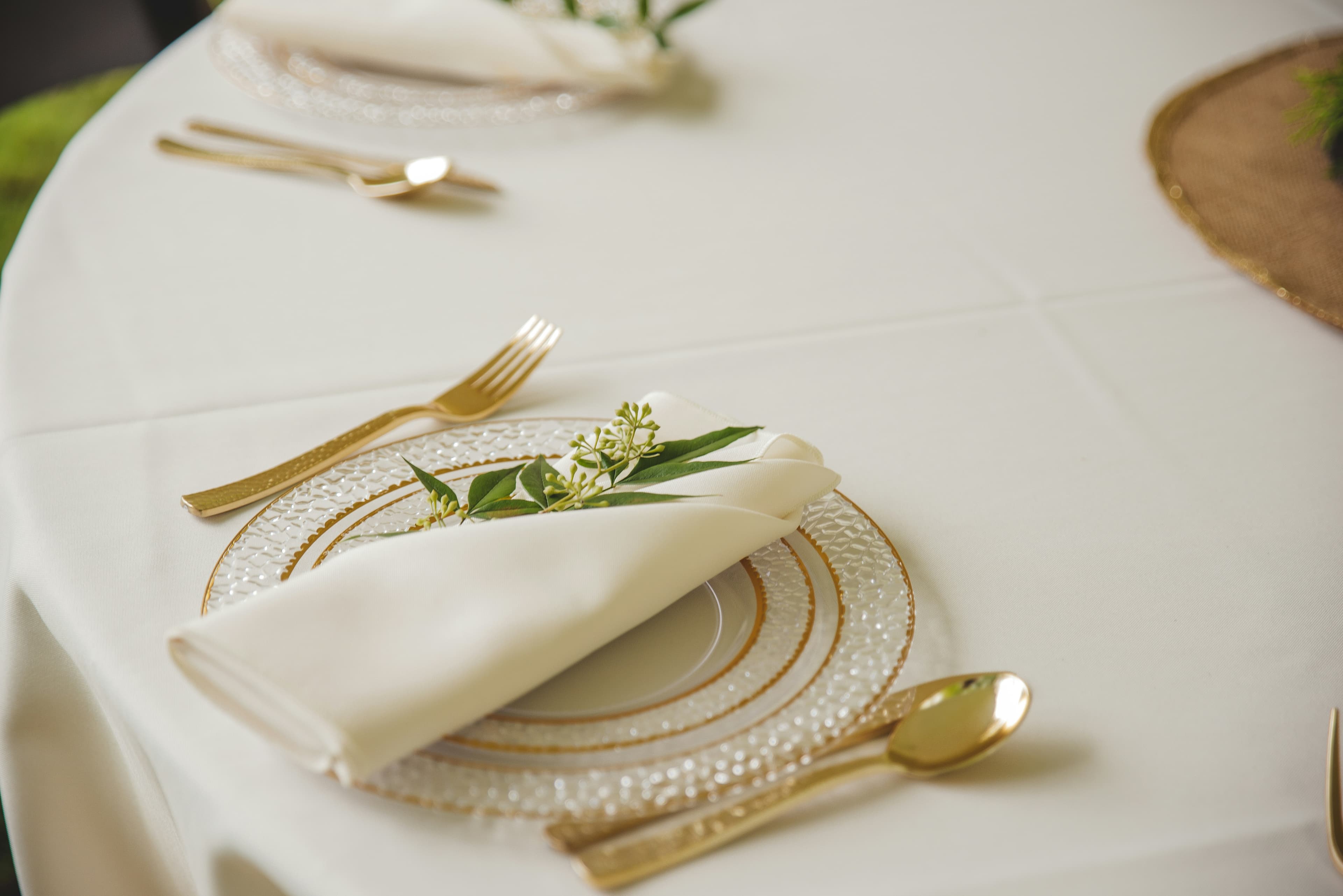 A folded linen napkin with gold cutlery and a sprig of greenery