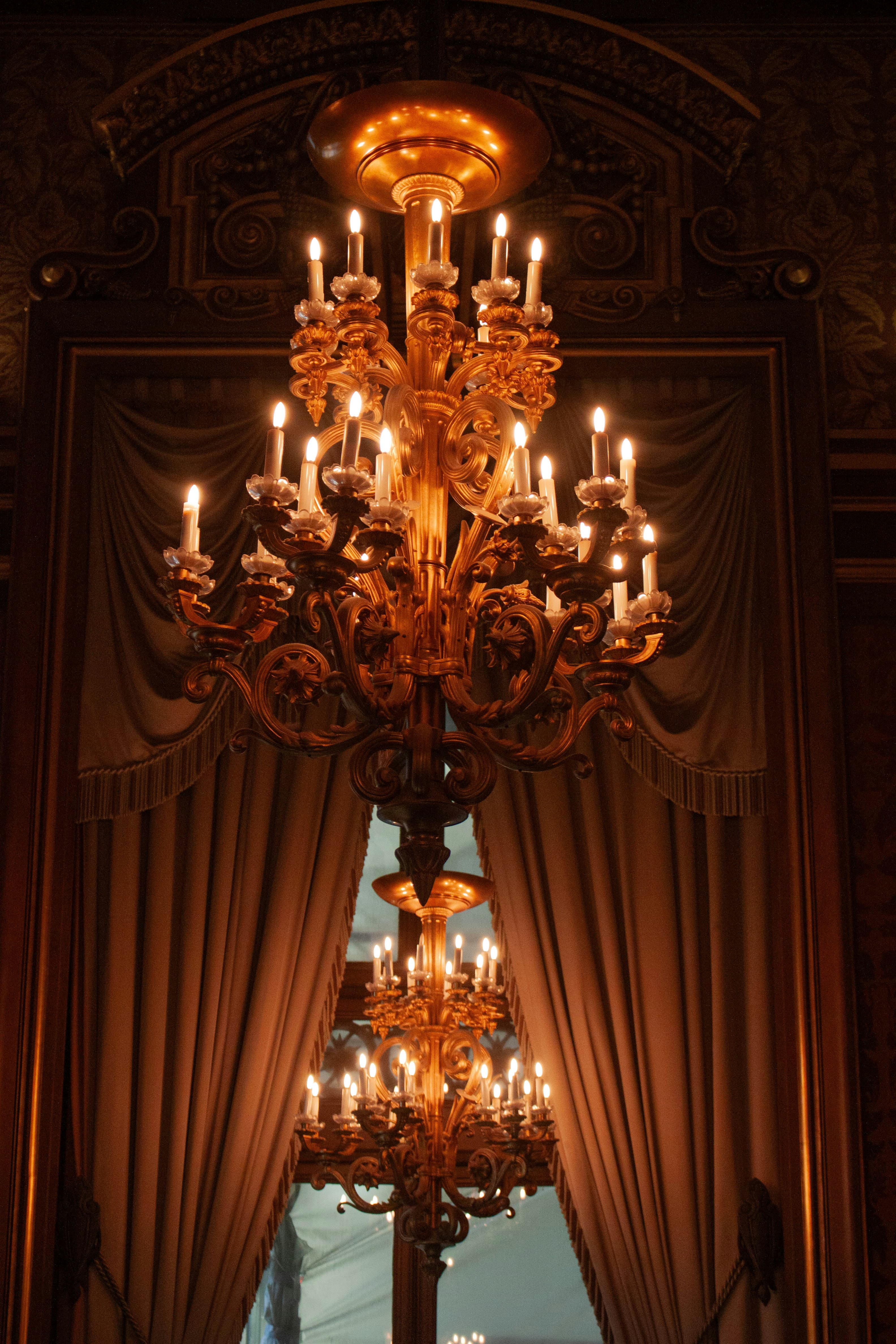 A gilded chandelier with lit candles against deep red drapes